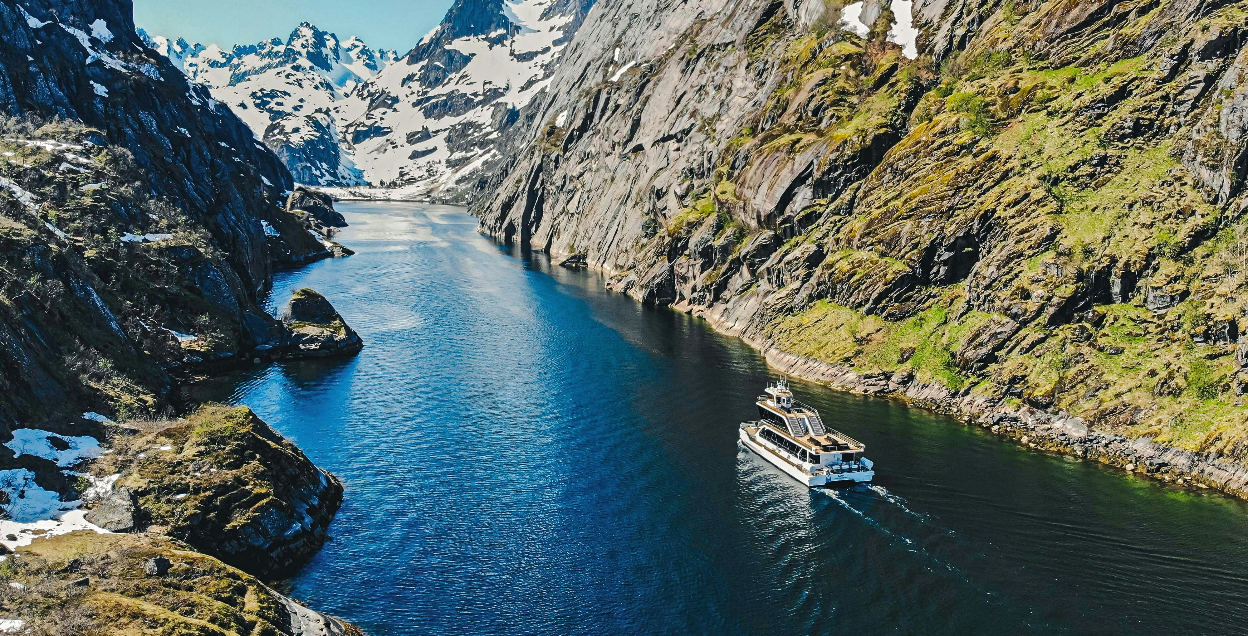 Cruise ship navigating Trollfjord's narrow passage in Lofoten, surrounded by steep cliffs and snowy peaks.