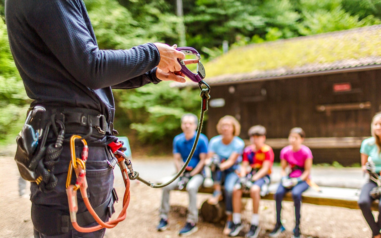 Instructor demonstrating safety gear at Ropes Park Interlaken to a seated group.