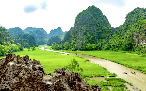 Boats on a river surrounded by lush green mountains in Tam Coc, Vietnam.