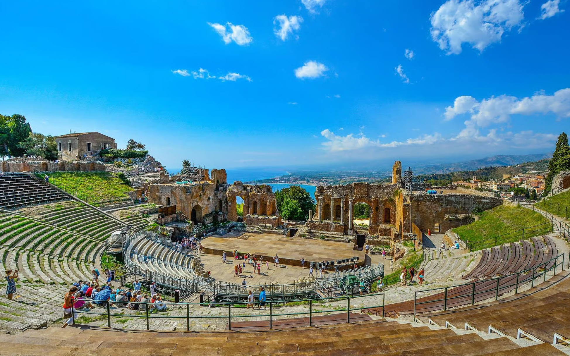 Taormina Ancient Theatre with coastal view and visitors exploring the historic site.
