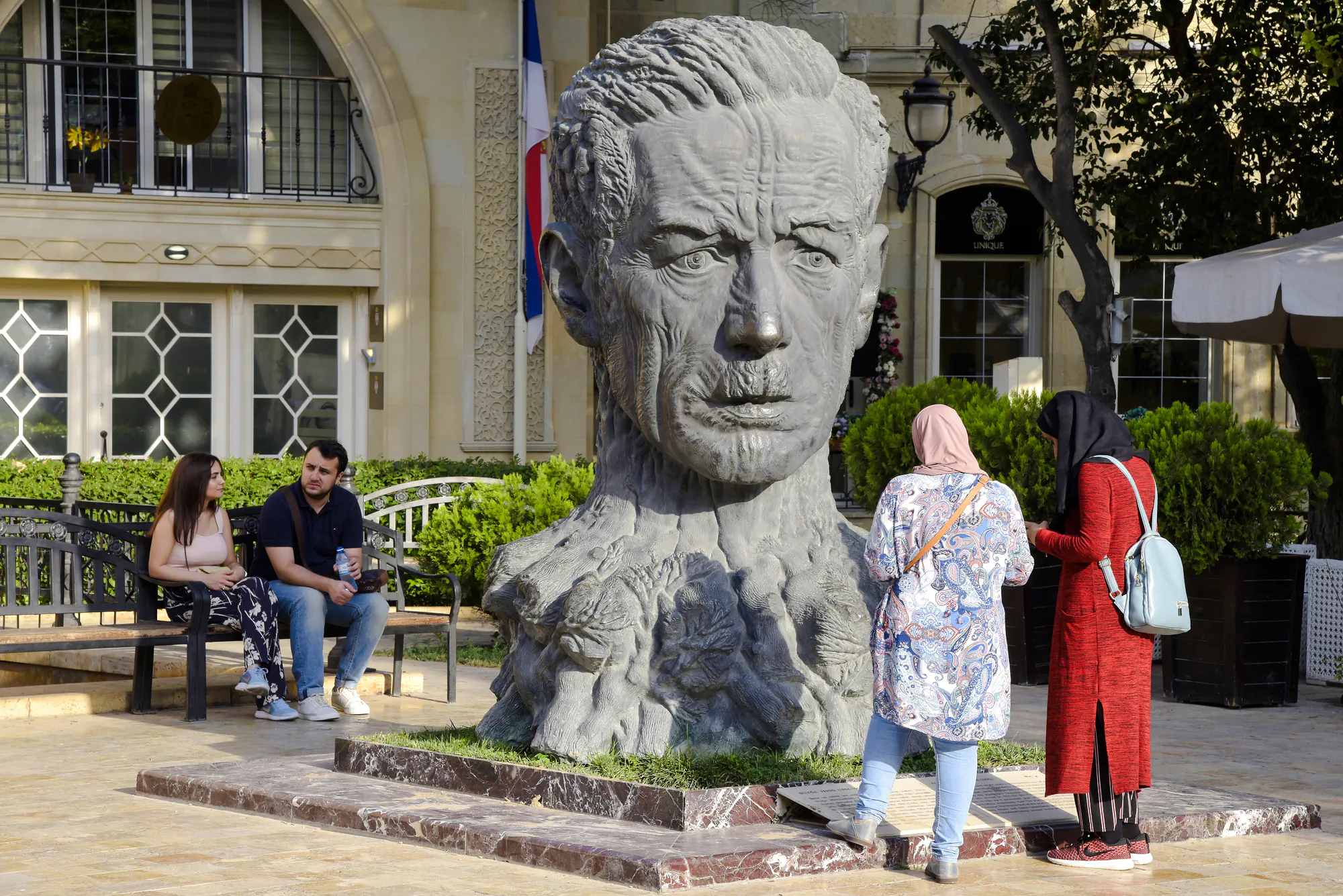Bust of a man in a Baku courtyard with visitors nearby, Old and Modern Baku City Tour.