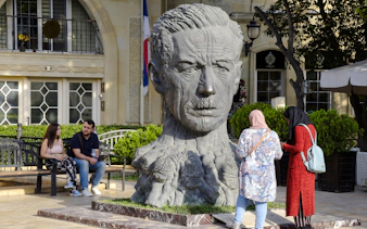 Bust of a man in a Baku courtyard with visitors nearby, Old and Modern Baku City Tour.