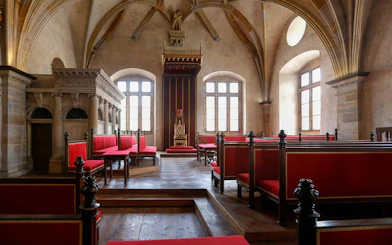 Interior of a historic hall with red seating and ornate throne in Prague Castle, Czech Republic.