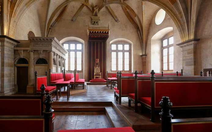 Interior of a historic hall with red seating and ornate throne in Prague Castle, Czech Republic.