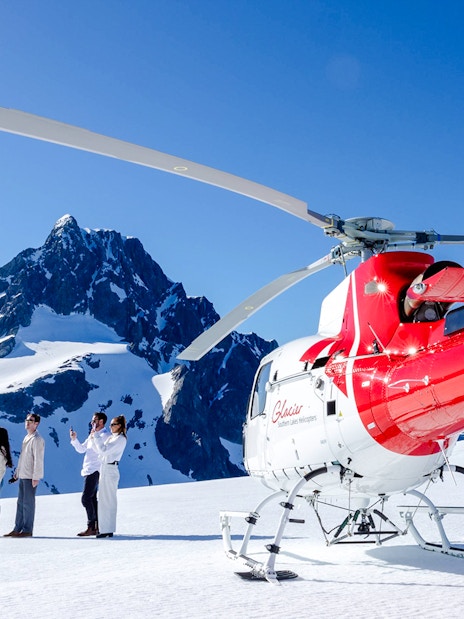 Four people beside a red and white helicopter on a snowy peak in Milford Sound.
