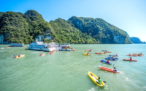 Canoes near a tour boat in Phang Bay, surrounded by lush cliffs, Phuket.
