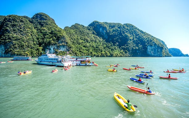 Canoes near a tour boat in Phang Bay, surrounded by lush cliffs, Phuket.