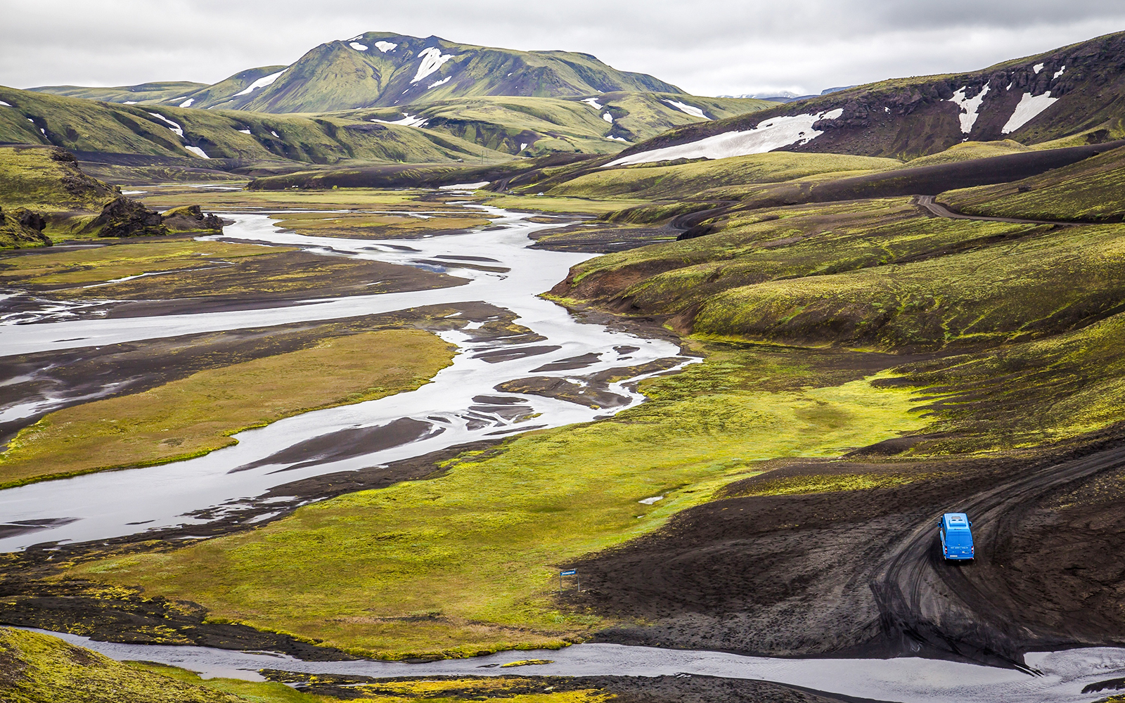 Blue vehicle on a winding road through the green and black landscape of Öskjuhlíð Hill, Iceland.