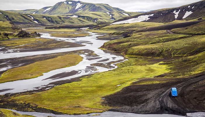 Blue vehicle on a winding road through the green and black landscape of Öskjuhlíð Hill, Iceland.