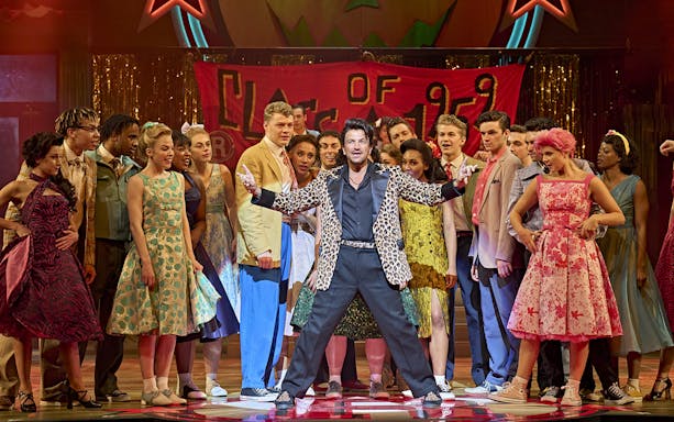 Cast of Grease musical performing on stage with a "Class of 1959" banner.
