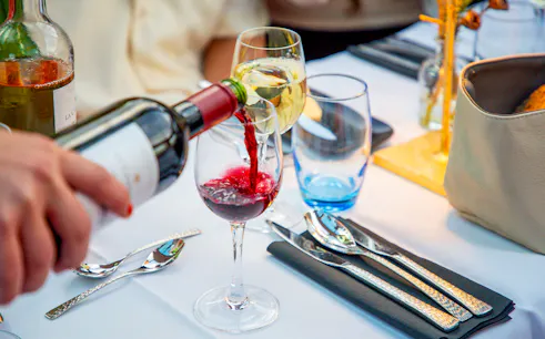 Wine being poured into a glass on an Amsterdam cruise table setting.
