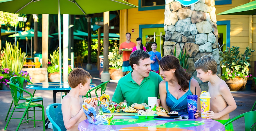 Family dining outdoors at Aquatica Orlando with colorful umbrellas and food trays.