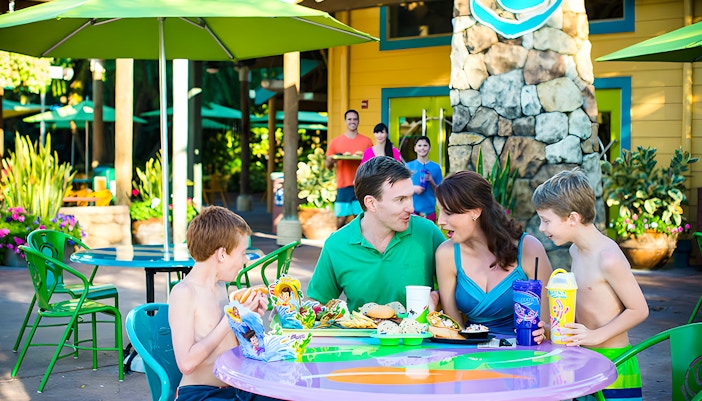 Family dining outdoors at Aquatica Orlando with colorful umbrellas and food trays.