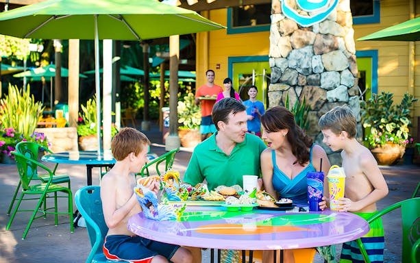 Family dining outdoors at Aquatica Orlando with colorful umbrellas and food trays.