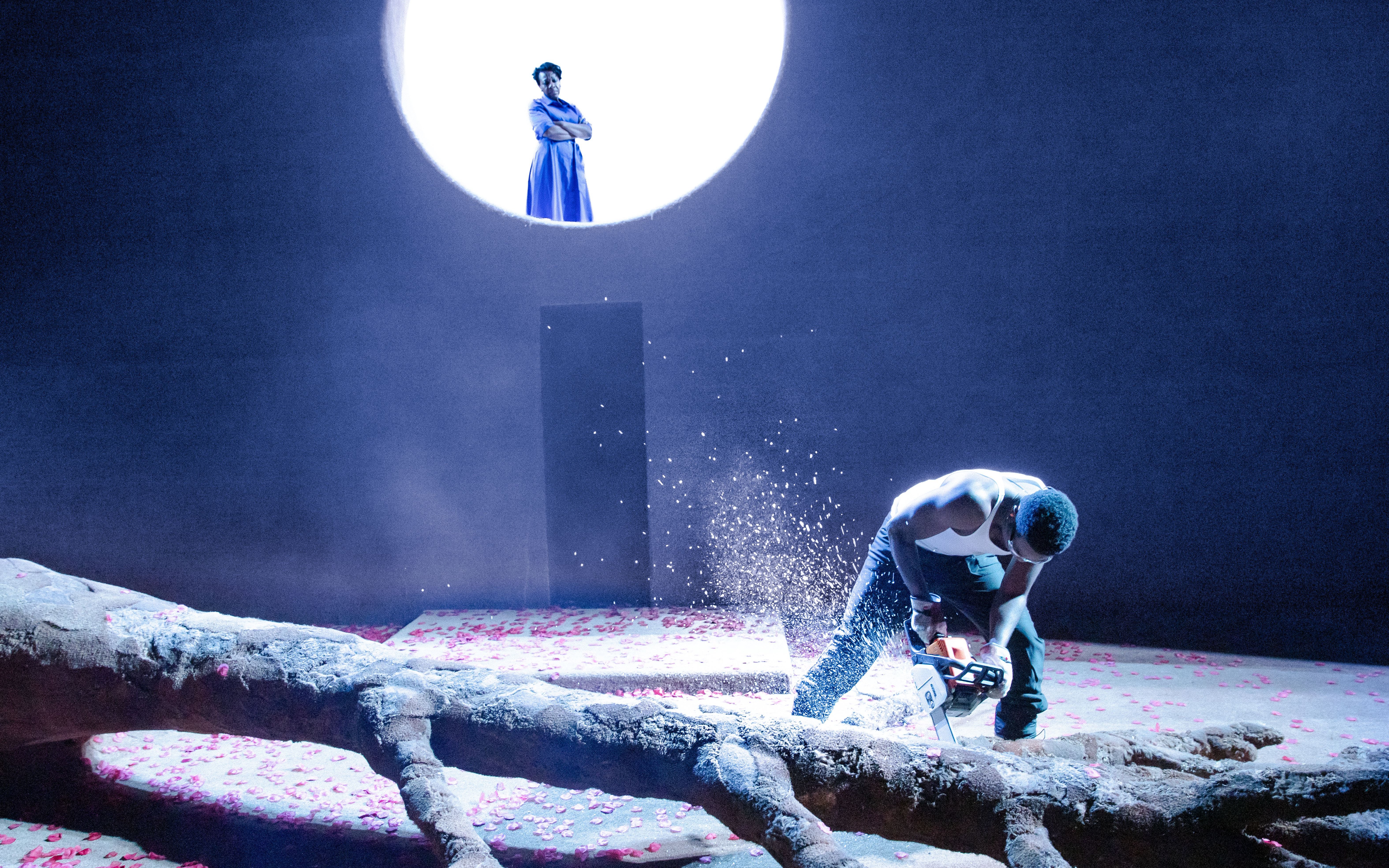 Stage scene from All My Sons West End show with actor using chainsaw on tree trunk.