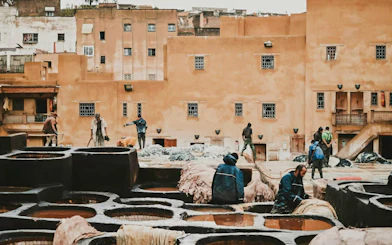 Workers at a traditional tannery in Fes, Morocco, with leather dyeing pits in the foreground.