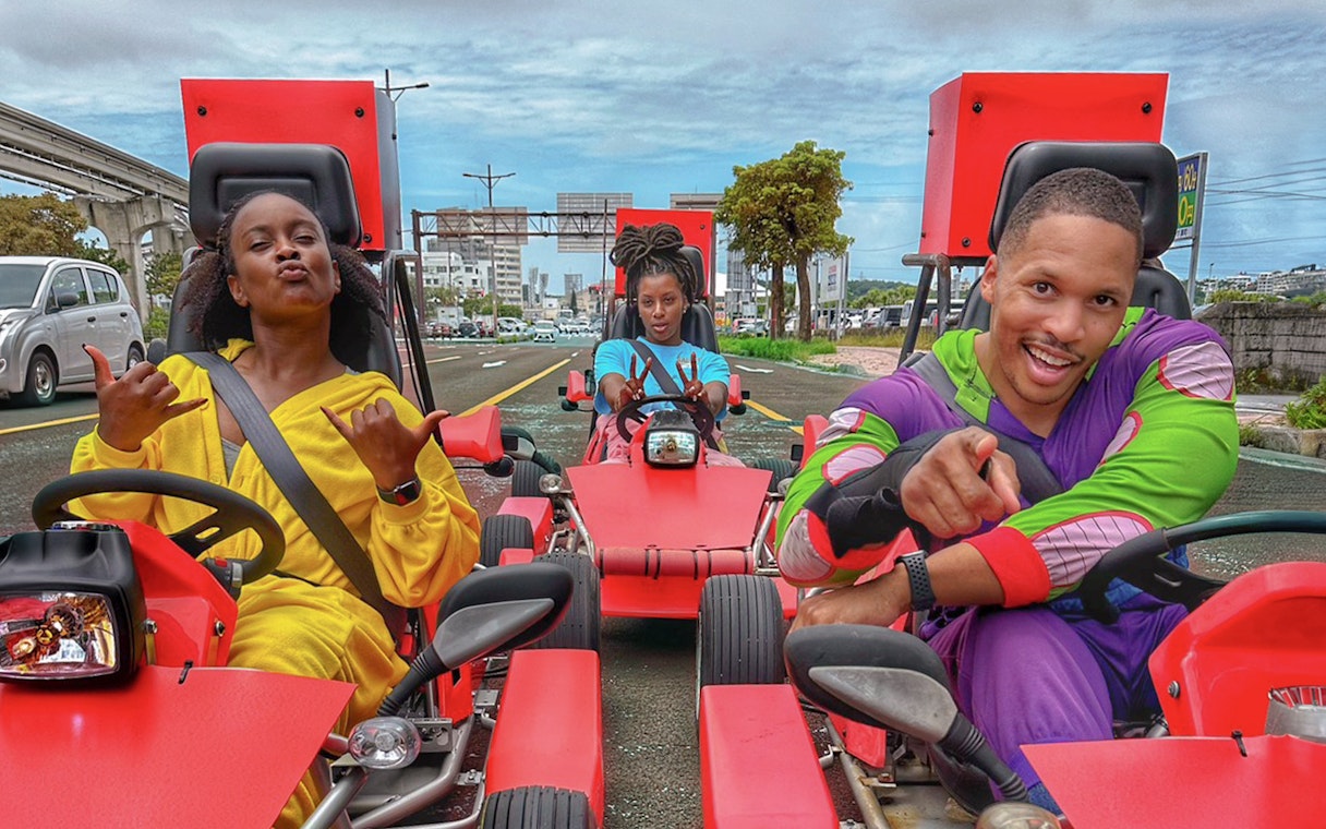 Street go-karting in Okinawa with three people in colorful outfits driving on a city road.