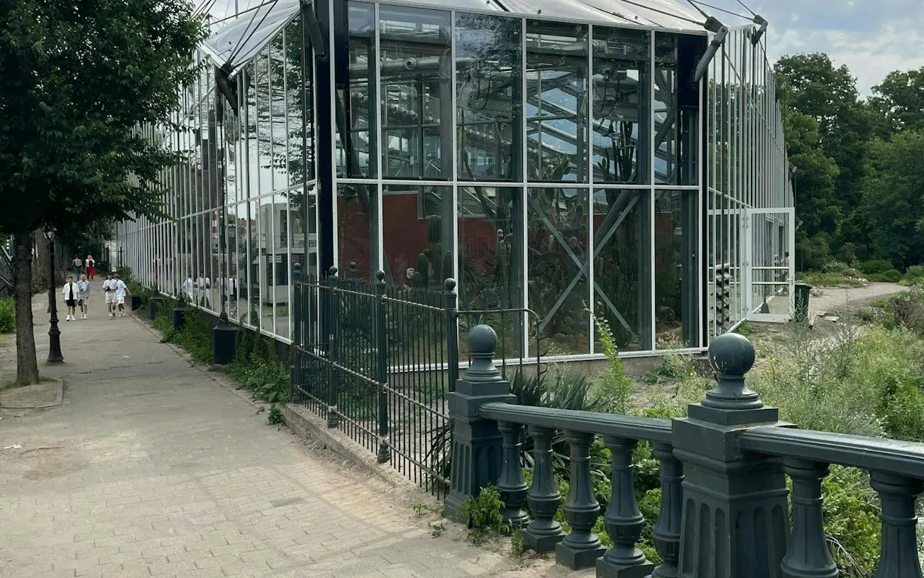 Glass greenhouse along a path in Amsterdam's Plantage district, part of a self-guided city exploration game.