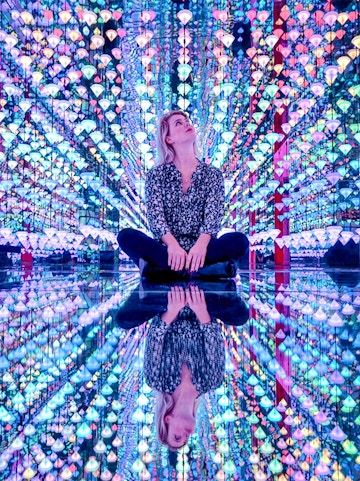 Person sitting in colorful light installation at Moco Museum Amsterdam exhibit.