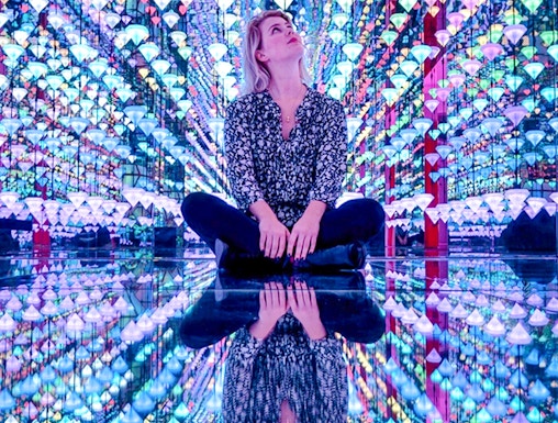 Person sitting in colorful light installation at Moco Museum Amsterdam exhibit.