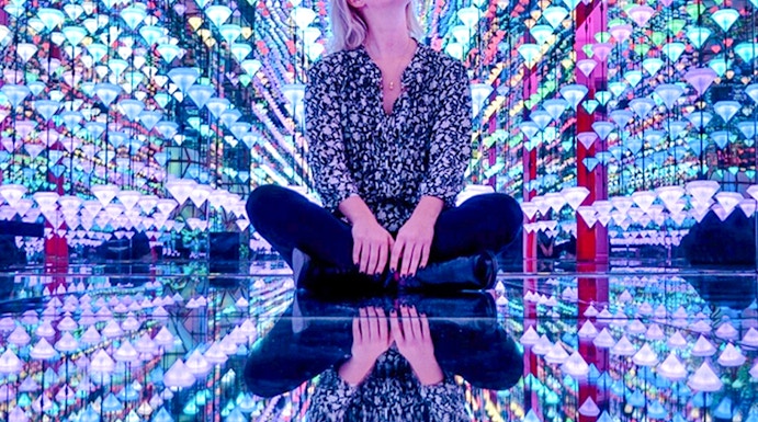 Person sitting in colorful light installation at Moco Museum Amsterdam exhibit.