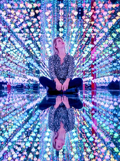 Person sitting in colorful light installation at Moco Museum Amsterdam exhibit.