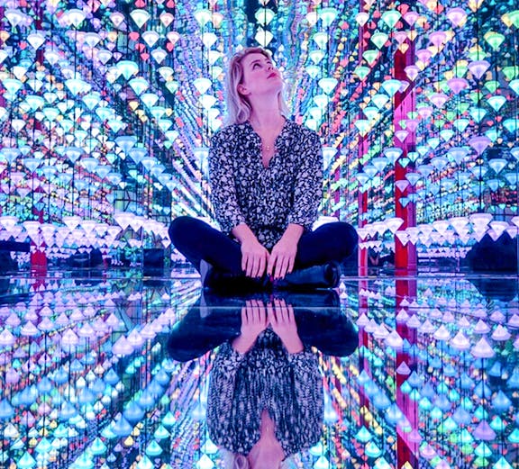 Person sitting in colorful light installation at Moco Museum Amsterdam exhibit.