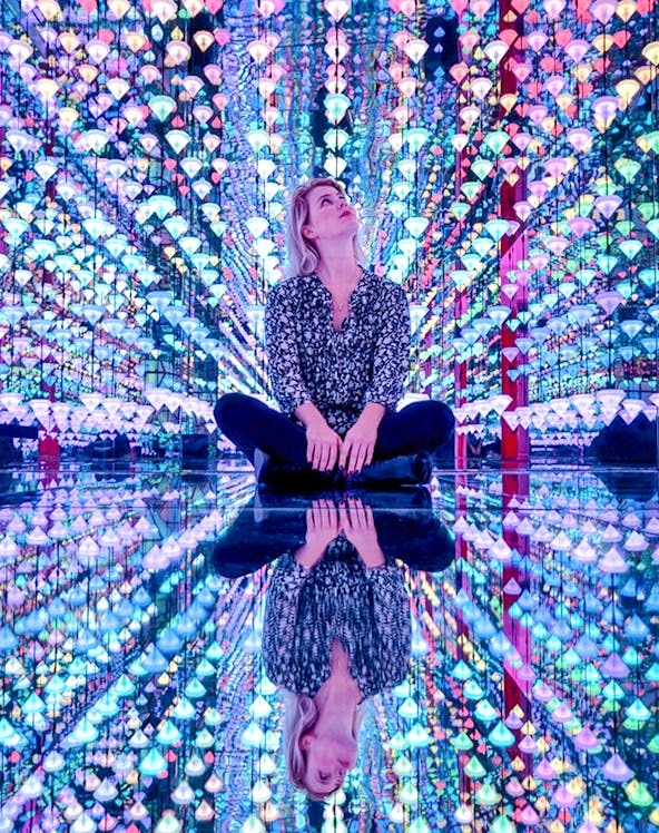 Person sitting in colorful light installation at Moco Museum Amsterdam exhibit.