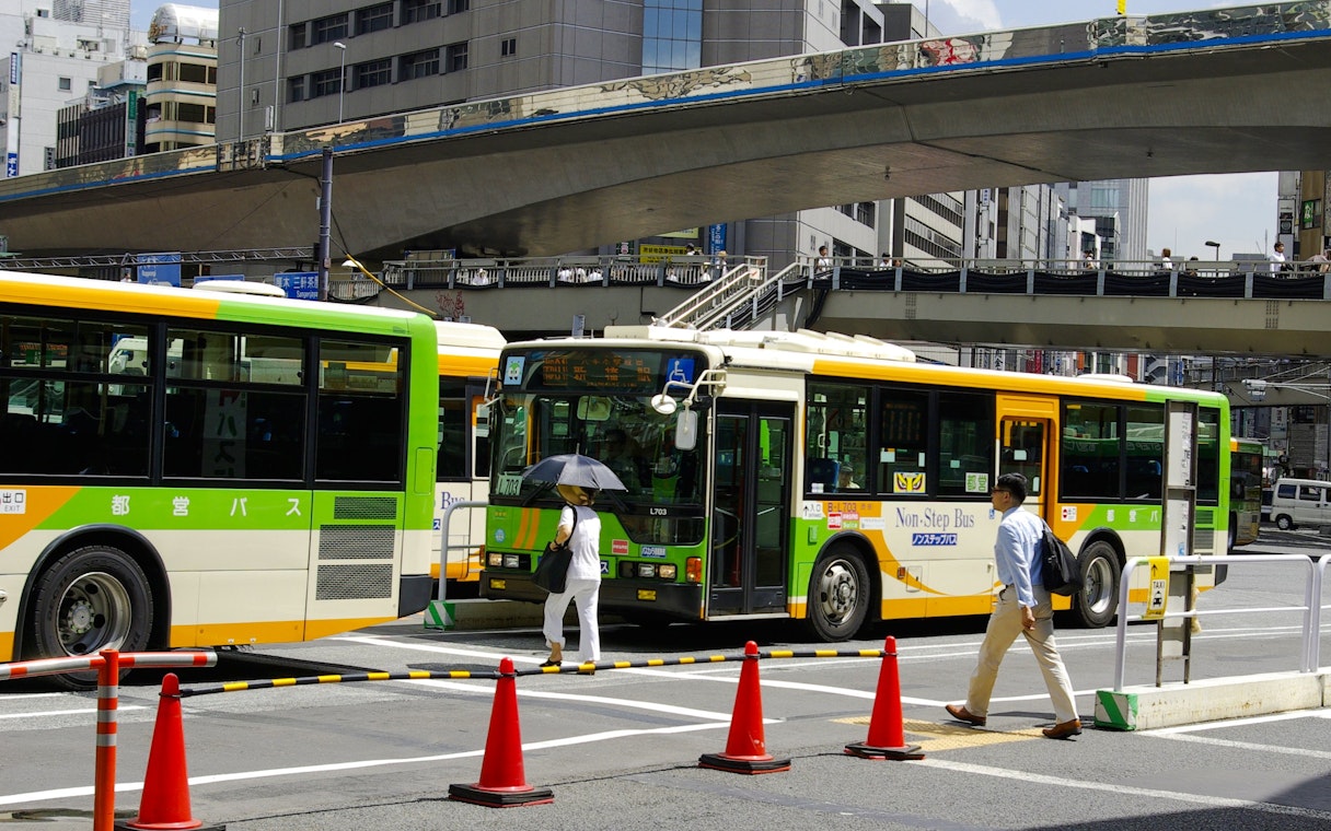 Public buses and pedestrians at a busy intersection in Osaka, Japan.