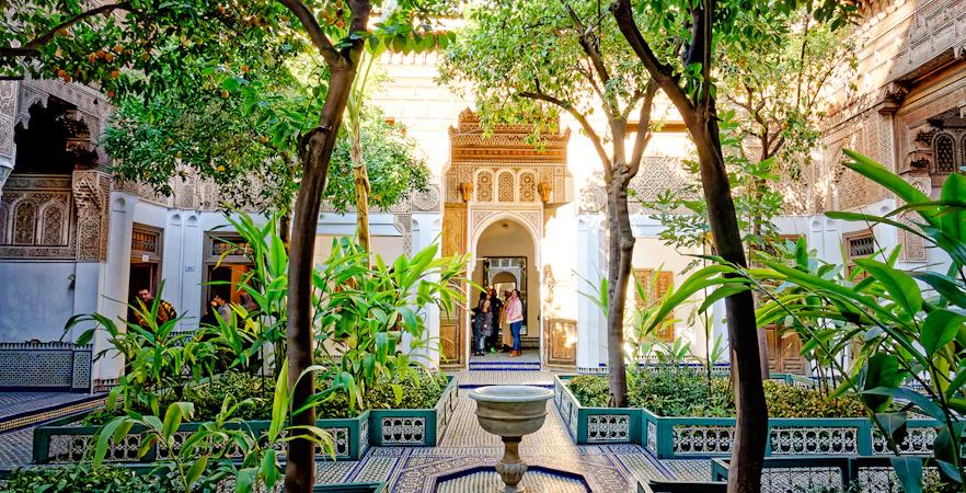 Bahia Palace courtyard with lush greenery and intricate archway in Marrakech, Morocco.
