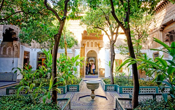 Bahia Palace courtyard with lush greenery and intricate archway in Marrakech, Morocco.