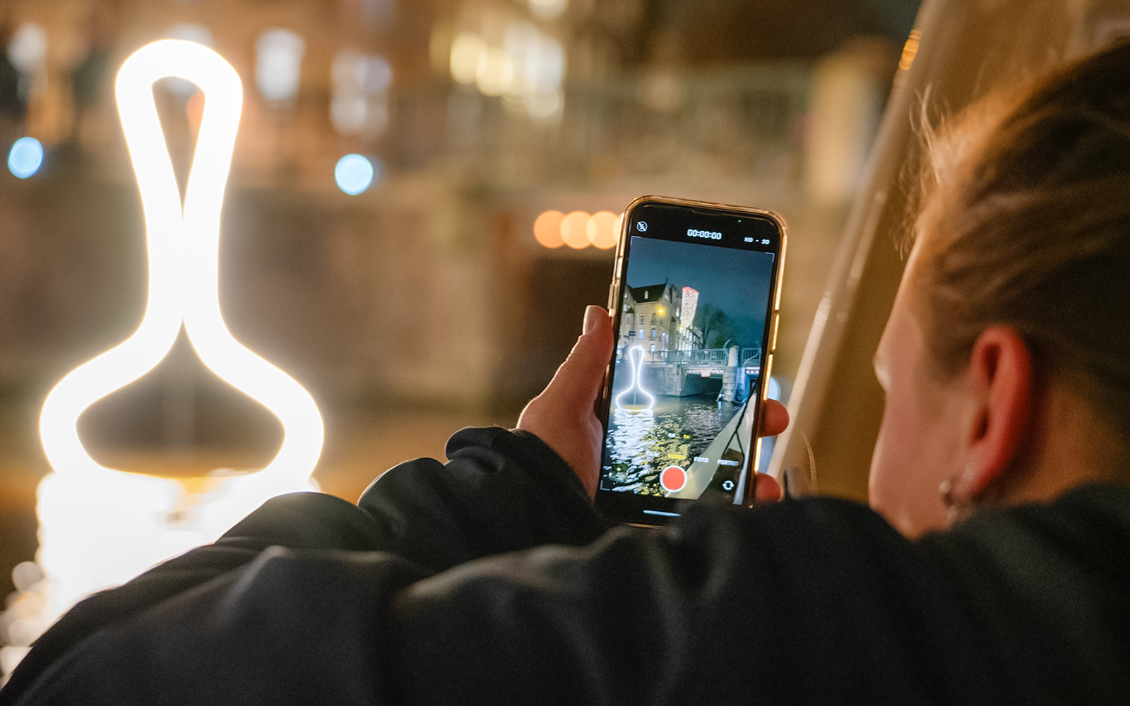 Person capturing Amsterdam Light Festival installation from a boat during a canal cruise.