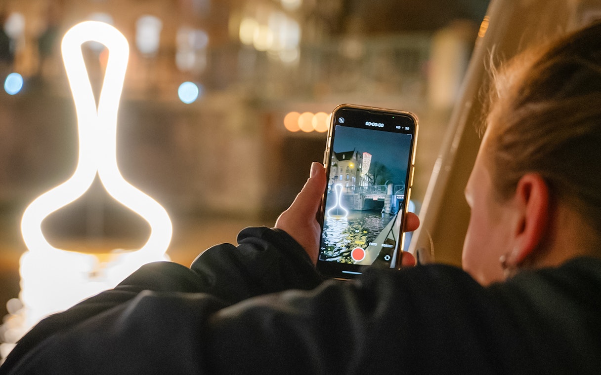 Person capturing Amsterdam Light Festival installation from a boat during a canal cruise.