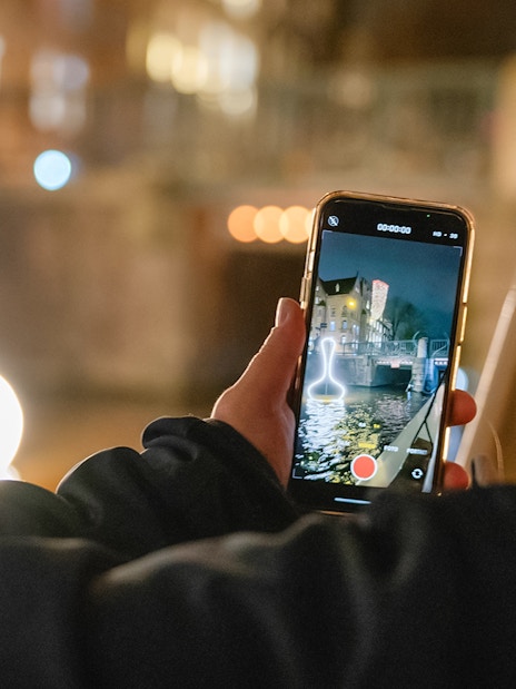 Person capturing Amsterdam Light Festival installation from a boat during a canal cruise.