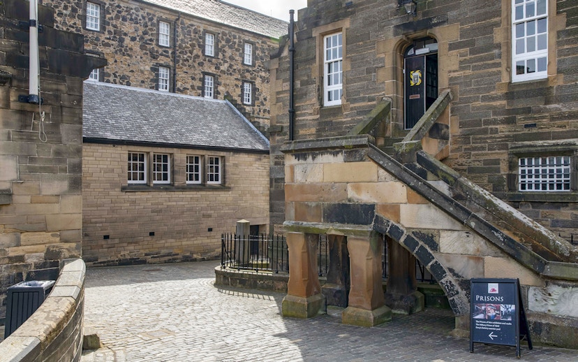 Edinburgh Castle courtyard with historic stone buildings and prison sign.