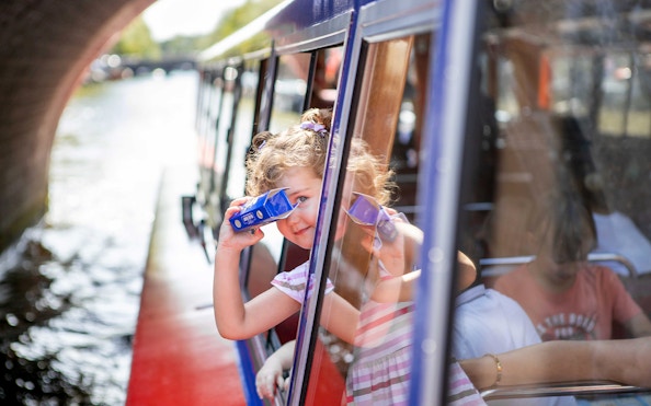 Child looking through binoculars on Amsterdam canal cruise.