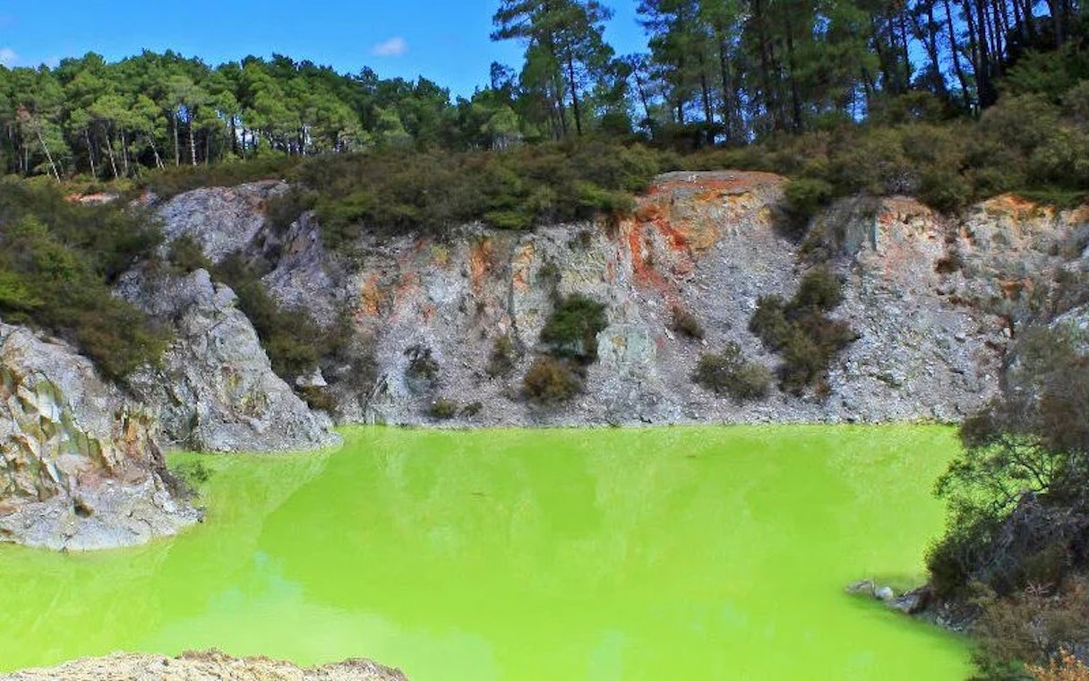 Wai-O-Tapu Thermal Wonderland's vibrant green geothermal pool surrounded by rocky cliffs.