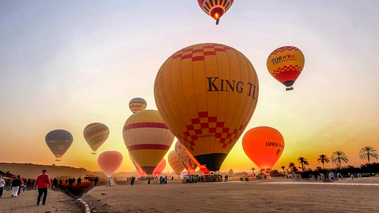 Hot air balloons ascending at sunrise in Luxor, Egypt, with people preparing for a ride.