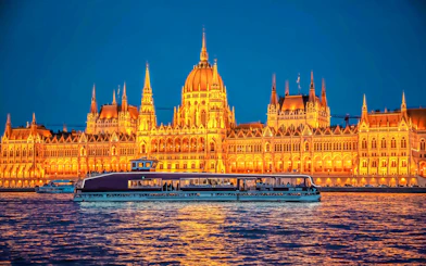 Budapest Parliament lit up at night with a cruise boat on the Danube River.