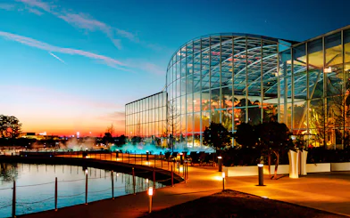 Therme Bucharest illuminated at night with glass facade reflecting sunset colors.
