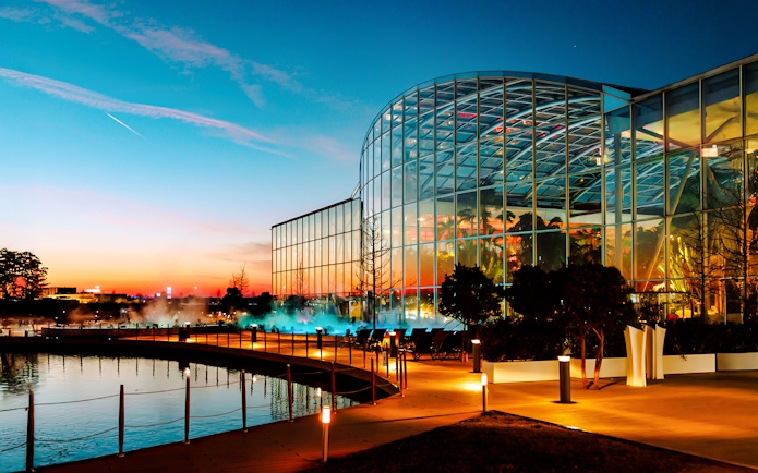 Therme Bucharest illuminated at night with glass facade reflecting sunset colors.