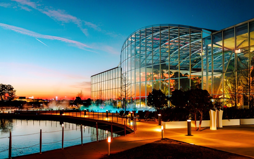 Therme Bucharest illuminated at night with glass facade reflecting sunset colors.