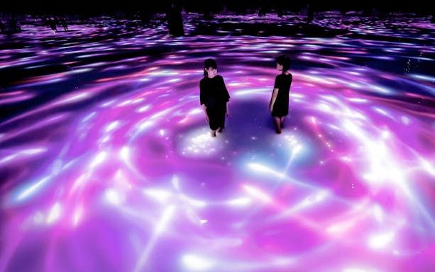 Visitors standing in illuminated water at teamLab Planets Tokyo exhibit.