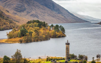 Glenfinnan Monument by Loch Shiel with autumn trees and mountains in the background.