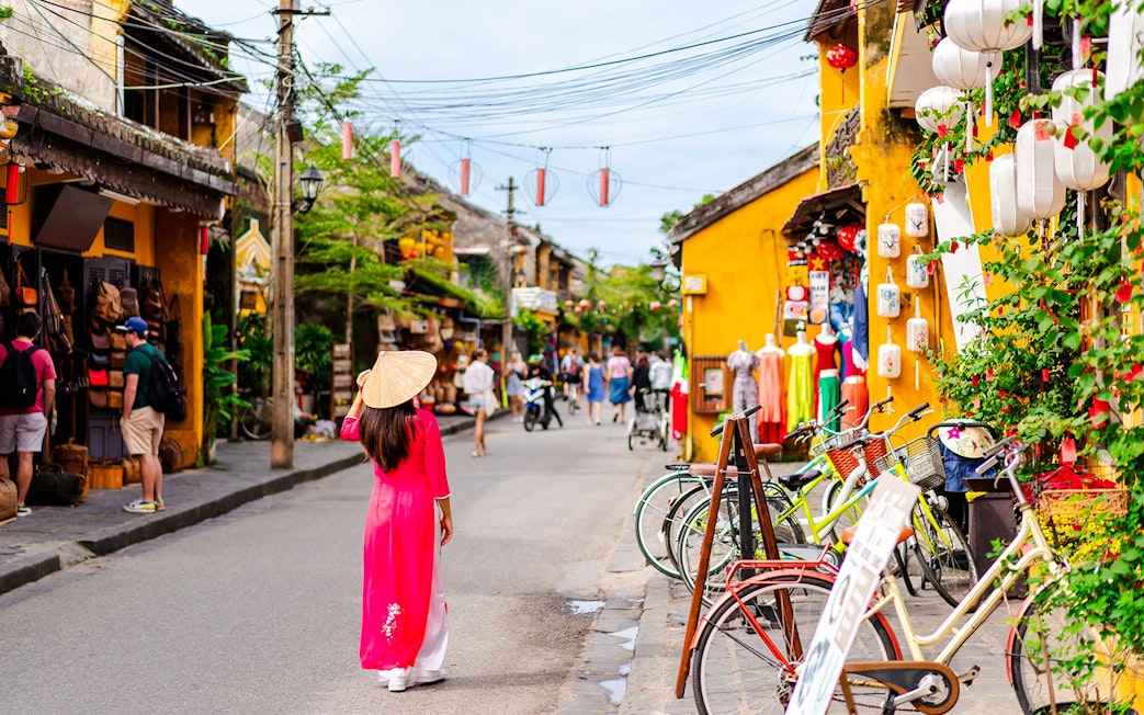Street scene in Hoi An Ancient Town, Vietnam, with a woman in traditional dress and colorful shops.