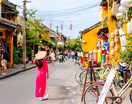 Street scene in Hoi An Ancient Town, Vietnam, with a woman in traditional dress and colorful shops.