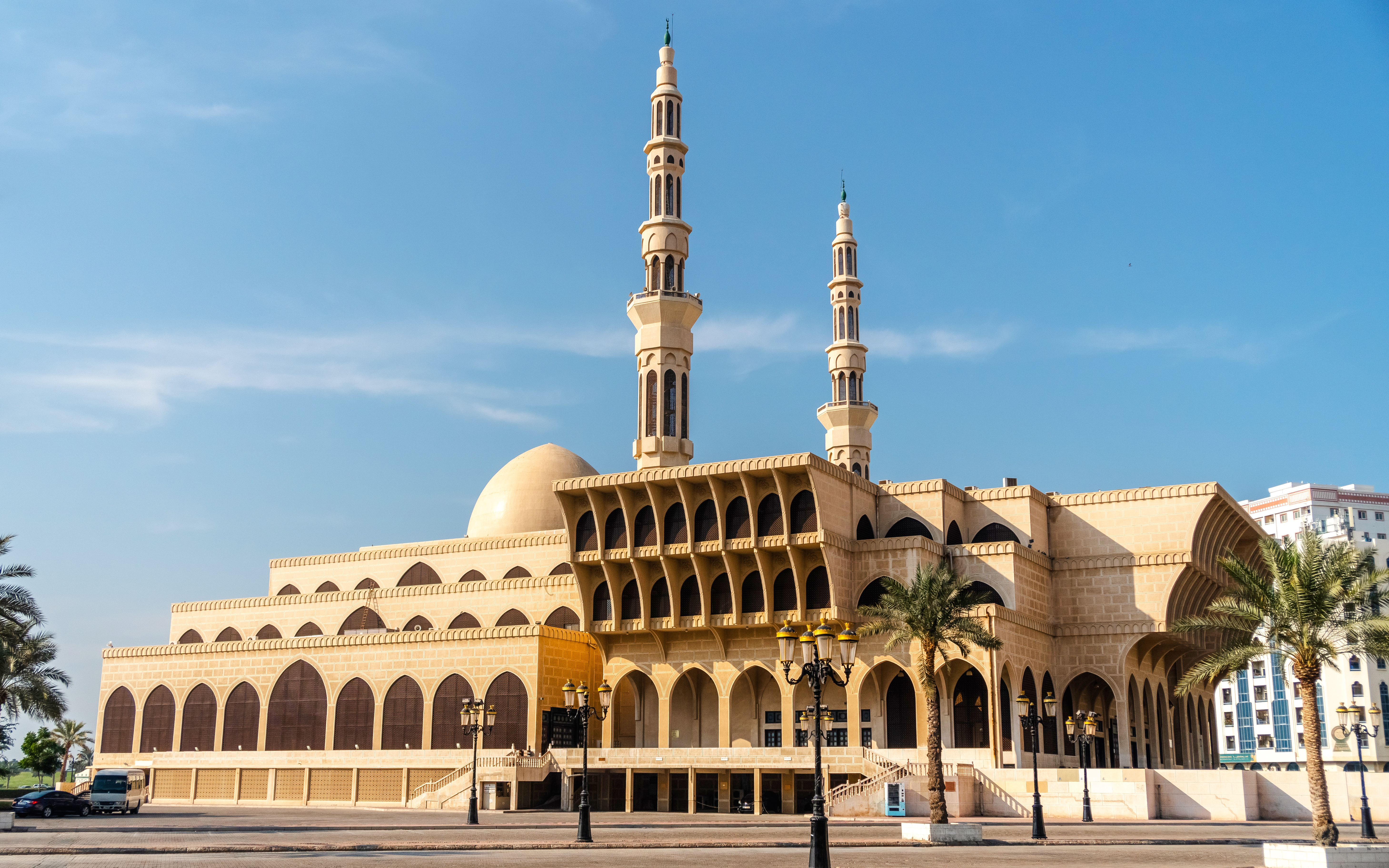Side view of King Faisal Mosque in Sharjah with two minarets and palm trees.