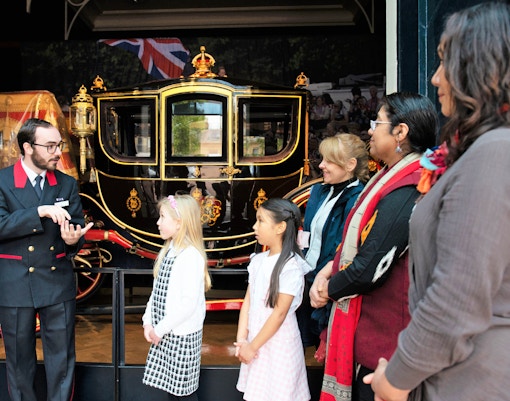 Tour guide explaining royal carriage to family at Buckingham Palace.