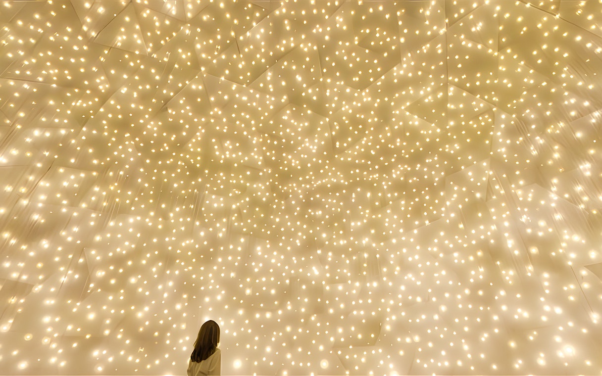 Person gazing at illuminated installation at TeamLab Phenomena Abu Dhabi.