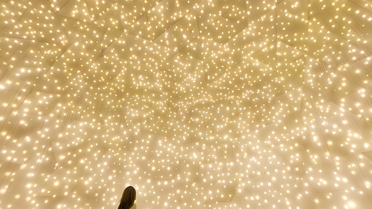 Person gazing at illuminated installation at TeamLab Phenomena Abu Dhabi.